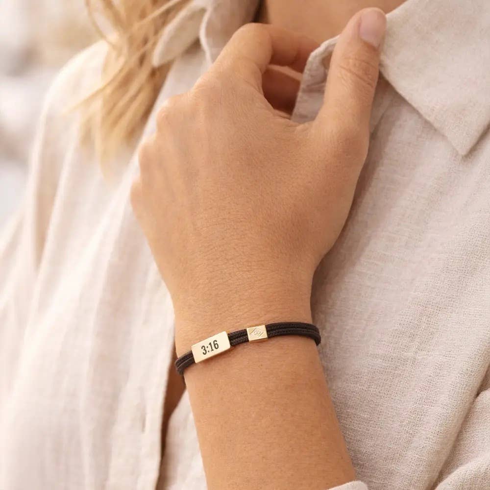 Hand wearing a bracelet with engraved text, against a neutral background