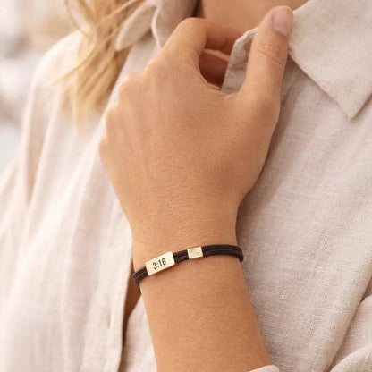 Hand wearing a bracelet with engraved text, against a neutral background