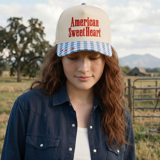 Person wearing a cap with 'American Sweetheart' text in a rural setting