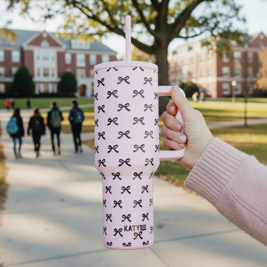 Hand holding a pink tumbler with purple bow pattern and 'KATYDID' branding.