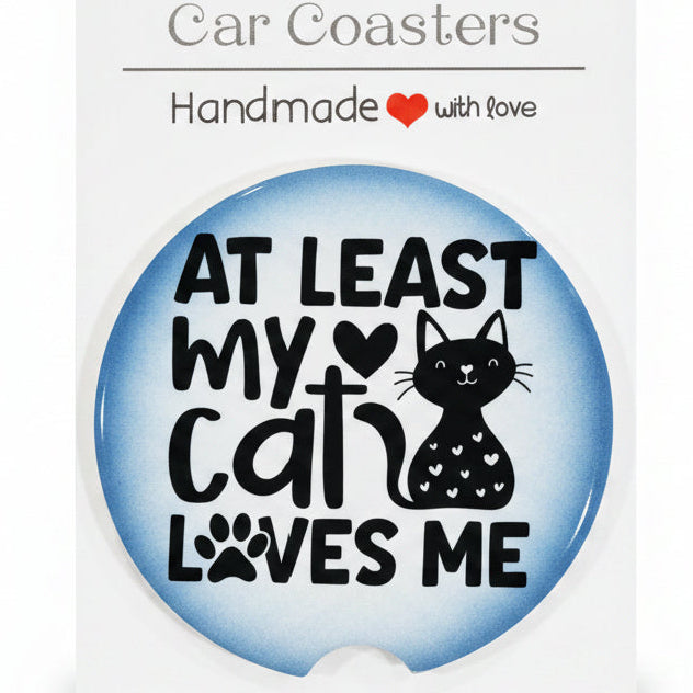 Car coaster with cat design and text on a white backing card, placed on a wooden surface.