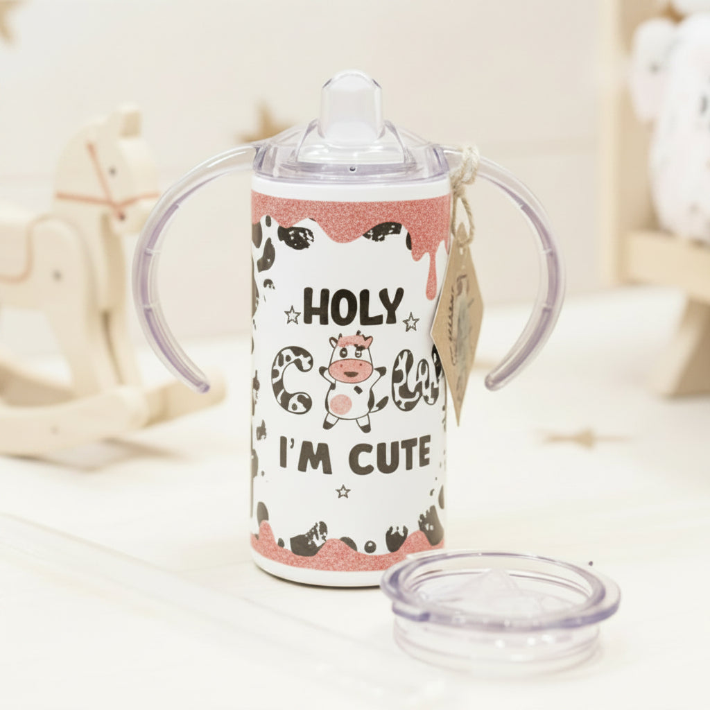 Children's sippy cup with cow design and text on a wooden surface