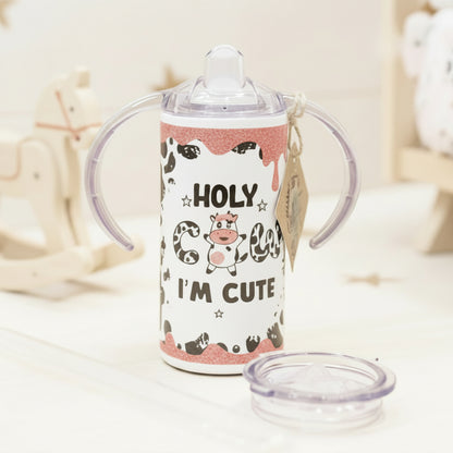 Children's sippy cup with cow design and text on a wooden surface
