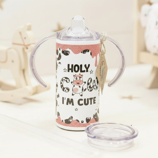 Children's sippy cup with cow design and text on a wooden surface