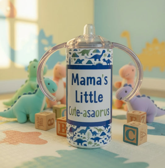 Children's sippy cup with dinosaur pattern and 'Mama's Little Cute-asaurus' text on the floor surrounded by baby toys